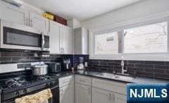 kitchen with sink, backsplash, white cabinets, and range with gas cooktop