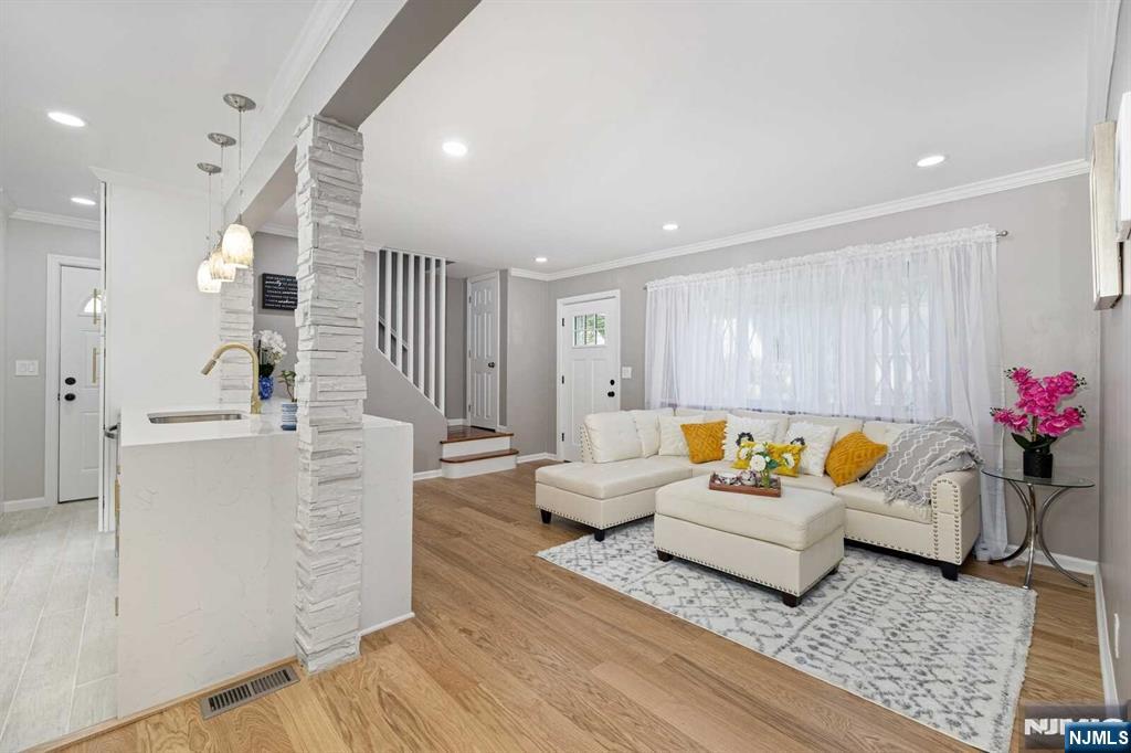 living room featuring ornate columns, crown molding, sink, and light wood-type flooring