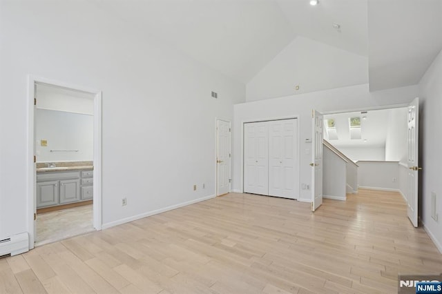 unfurnished bedroom featuring ensuite bathroom, high vaulted ceiling, a baseboard radiator, sink, and light wood-type flooring