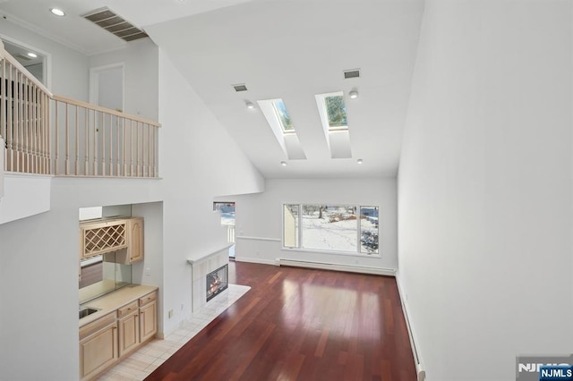 living room featuring a tile fireplace, a skylight, a high ceiling, hardwood / wood-style flooring, and baseboard heating