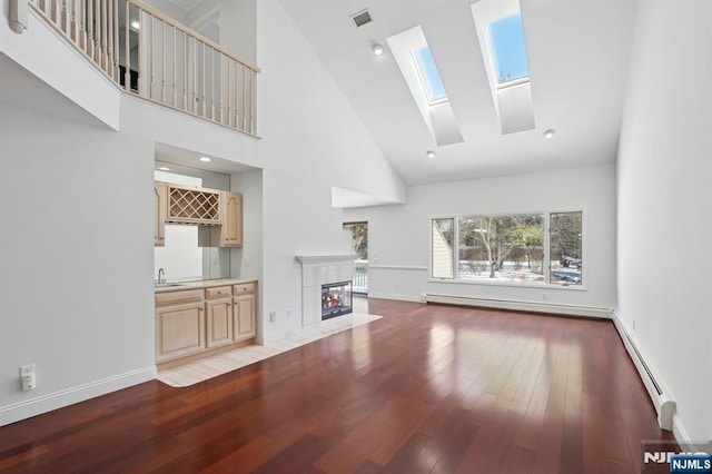 unfurnished living room featuring hardwood / wood-style floors, a baseboard radiator, a tiled fireplace, a high ceiling, and wet bar