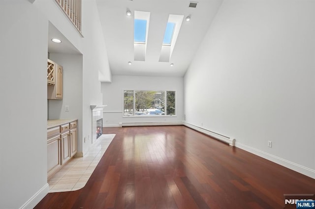 unfurnished living room featuring light wood-type flooring, a skylight, a high ceiling, and a baseboard heating unit