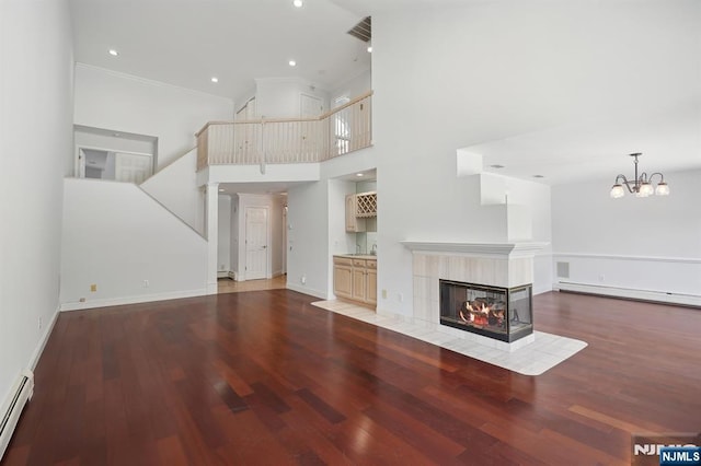 unfurnished living room with wood-type flooring, ornamental molding, a towering ceiling, and a fireplace