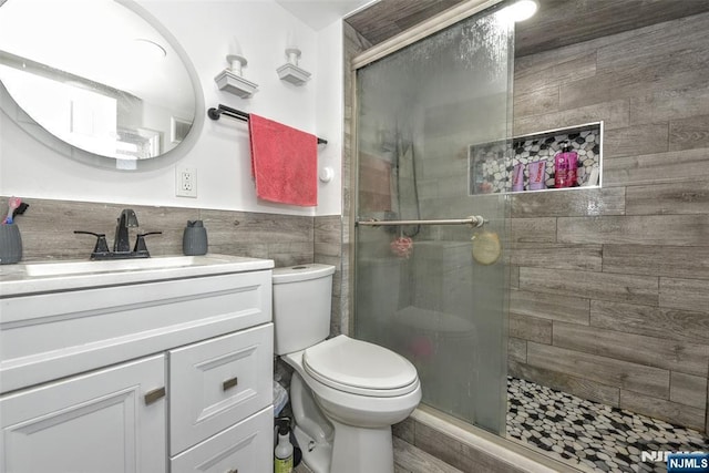 bathroom with tile walls, vanity, toilet, and an enclosed shower