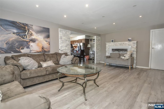 living room with a stone fireplace and light wood-type flooring