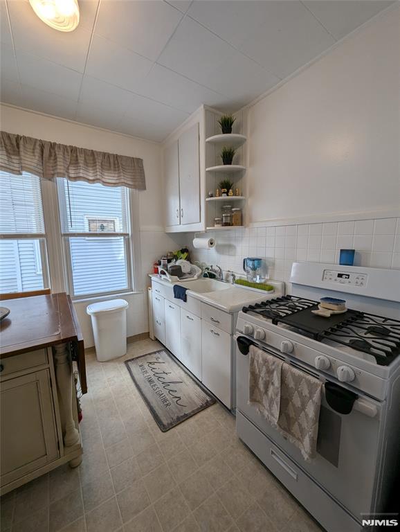 kitchen with sink, white range with gas stovetop, and tile walls