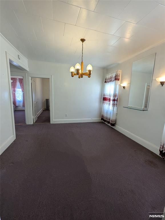 empty room with dark colored carpet and a notable chandelier