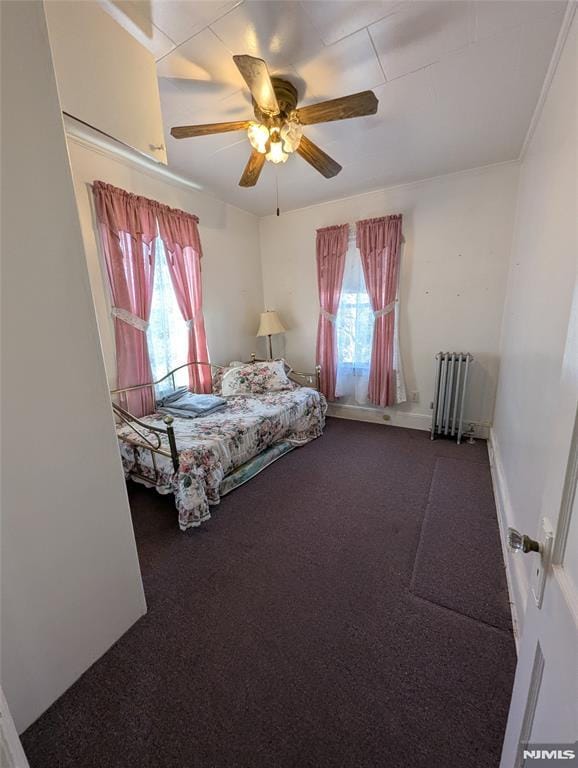 unfurnished bedroom featuring multiple windows, carpet floors, radiator heating unit, and ceiling fan