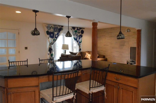 kitchen featuring decorative backsplash, a kitchen bar, hanging light fixtures, and ornate columns