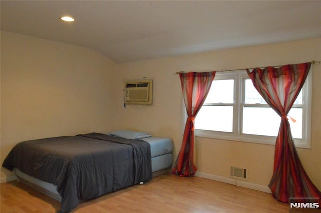 bedroom featuring vaulted ceiling, wood-type flooring, and a wall mounted air conditioner