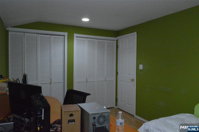 bedroom featuring wood-type flooring, vaulted ceiling, and two closets