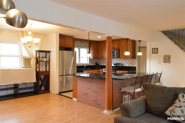 kitchen with pendant lighting, tasteful backsplash, a kitchen breakfast bar, light hardwood / wood-style floors, and stainless steel appliances