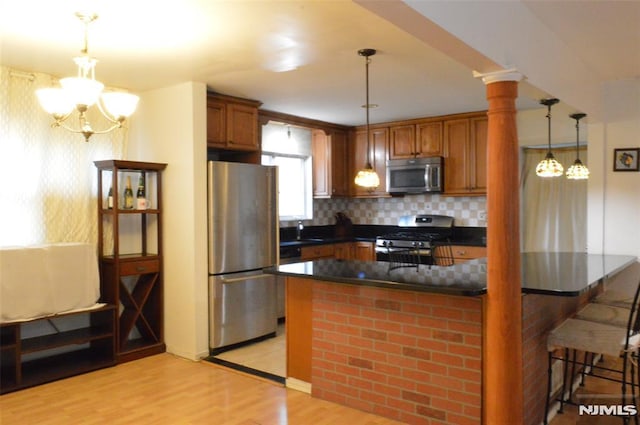 kitchen with a breakfast bar, stainless steel appliances, decorative backsplash, decorative light fixtures, and light wood-type flooring