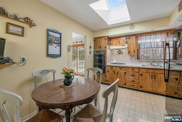 kitchen featuring tasteful backsplash, a skylight, light tile patterned floors, black double oven, and stainless steel gas stovetop