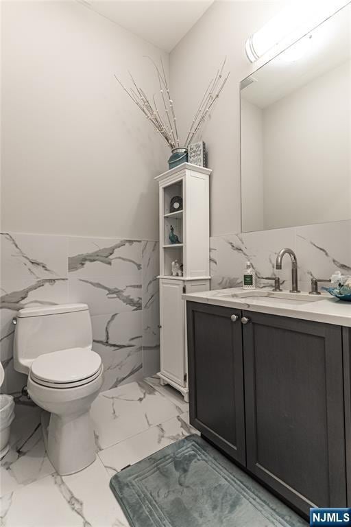 bathroom featuring vanity, tile walls, and toilet