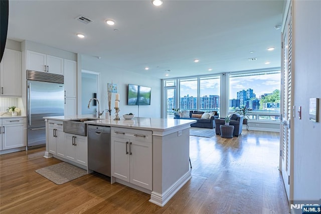 kitchen with light wood-type flooring, stainless steel appliances, a kitchen island with sink, and white cabinets