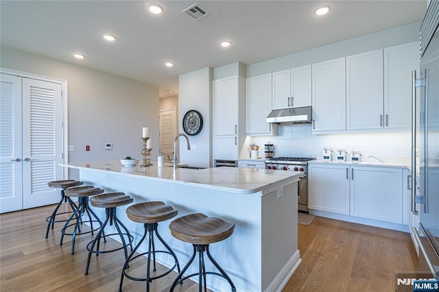 kitchen with stainless steel range, sink, an island with sink, and white cabinets