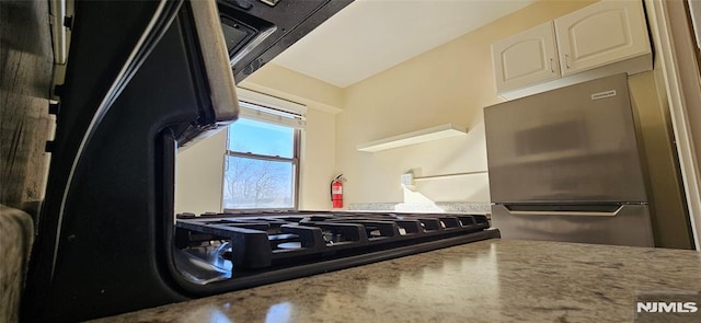 kitchen featuring stainless steel refrigerator, light stone counters, and white cabinets