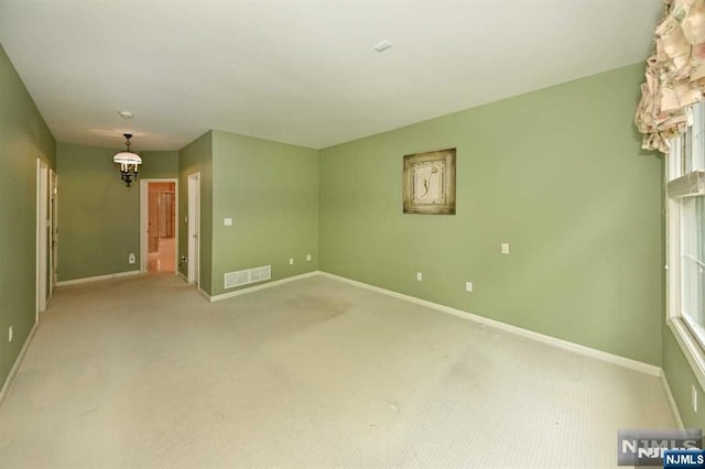 spare room featuring light carpet and a chandelier