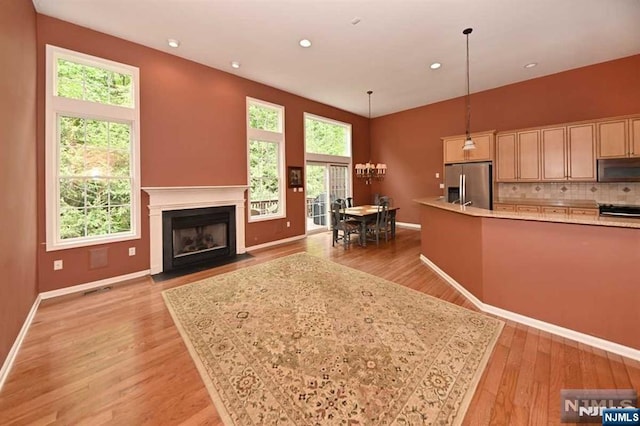 kitchen featuring tasteful backsplash, stainless steel fridge with ice dispenser, light hardwood / wood-style flooring, hanging light fixtures, and a center island with sink