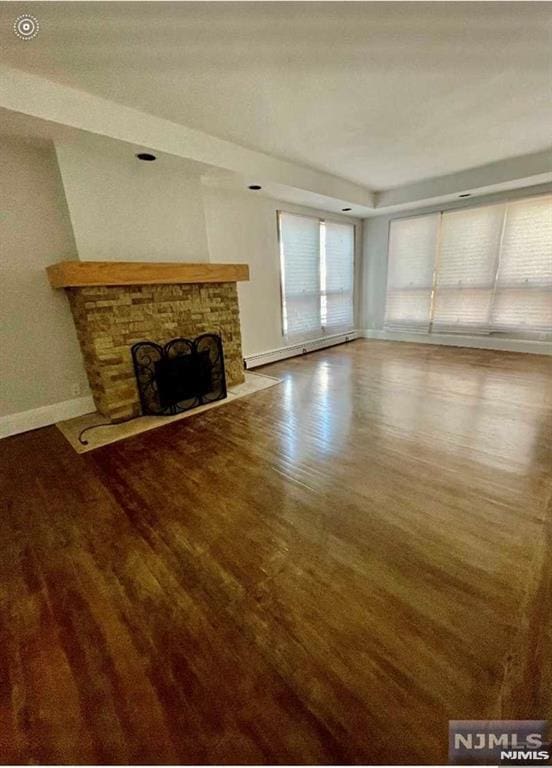 unfurnished living room with wood-type flooring, a stone fireplace, and a baseboard heating unit