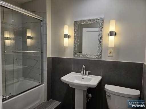 bathroom with bath / shower combo with glass door, tile walls, and toilet