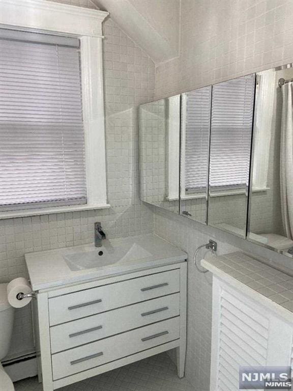 bathroom with vanity, a baseboard heating unit, tile walls, and a wealth of natural light