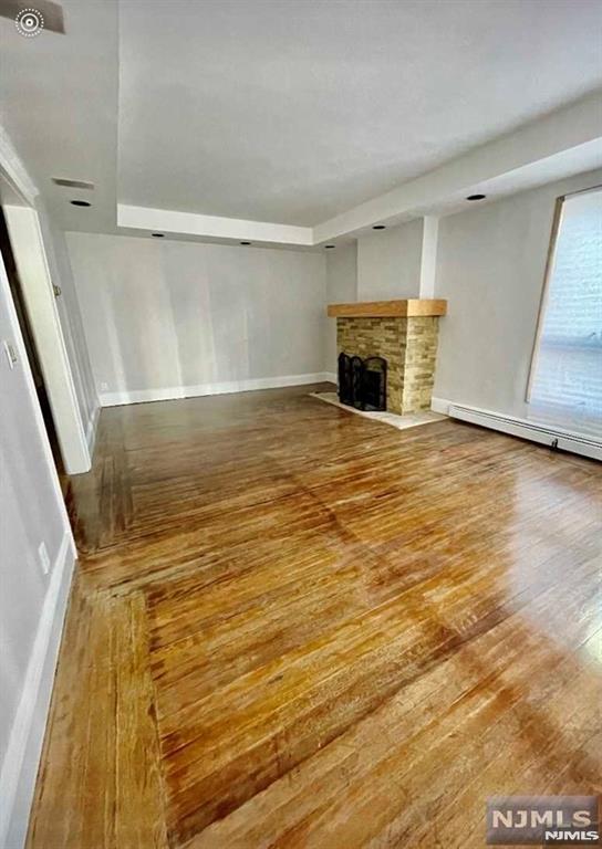 unfurnished living room with hardwood / wood-style flooring and a baseboard heating unit