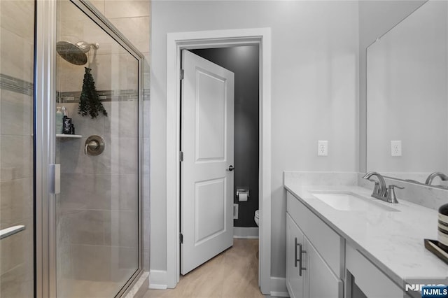 bathroom with a shower with door, vanity, wood-type flooring, and toilet