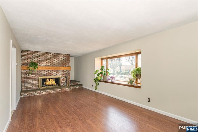 unfurnished living room with wood-type flooring and a brick fireplace