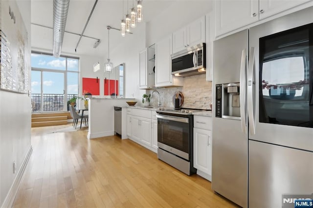 kitchen with appliances with stainless steel finishes, tasteful backsplash, white cabinetry, sink, and hanging light fixtures