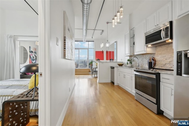 kitchen with sink, tasteful backsplash, hanging light fixtures, stainless steel appliances, and white cabinets