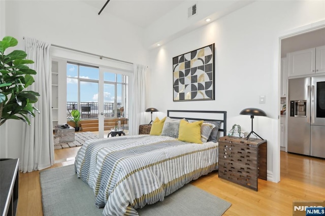 bedroom with access to exterior, stainless steel fridge, and light wood-type flooring