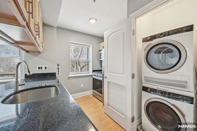 kitchen featuring stacked washer and dryer, sink, light hardwood / wood-style floors, and stainless steel appliances