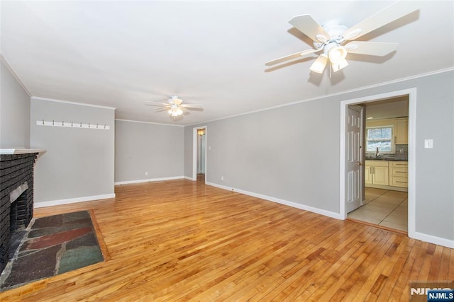 unfurnished living room with crown molding, ceiling fan, a brick fireplace, and light wood-type flooring