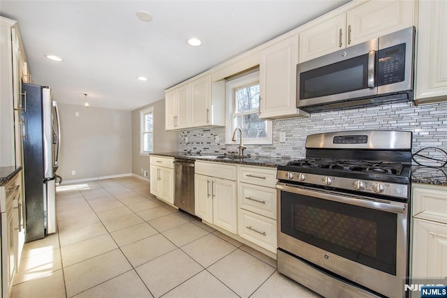 kitchen with sink, light tile patterned floors, appliances with stainless steel finishes, dark stone countertops, and tasteful backsplash