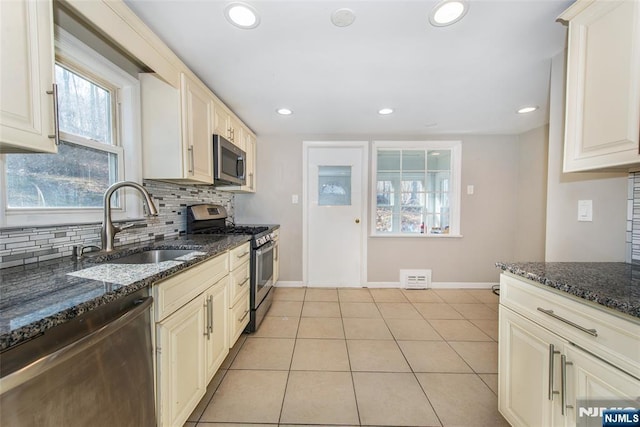 kitchen with sink, light tile patterned floors, appliances with stainless steel finishes, dark stone countertops, and decorative backsplash