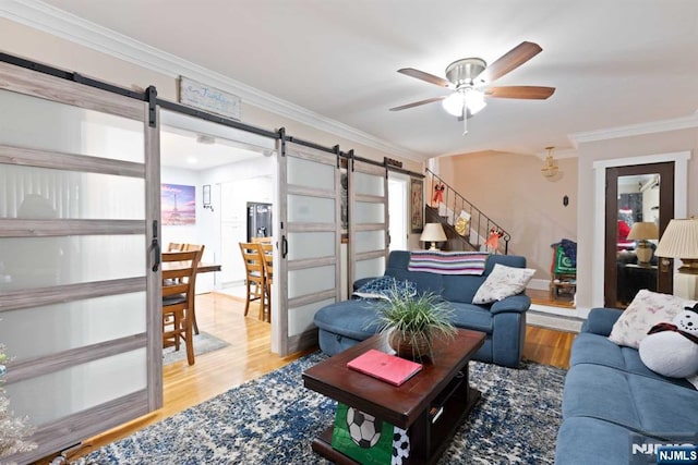 living room with crown molding, ceiling fan, wood-type flooring, and a barn door