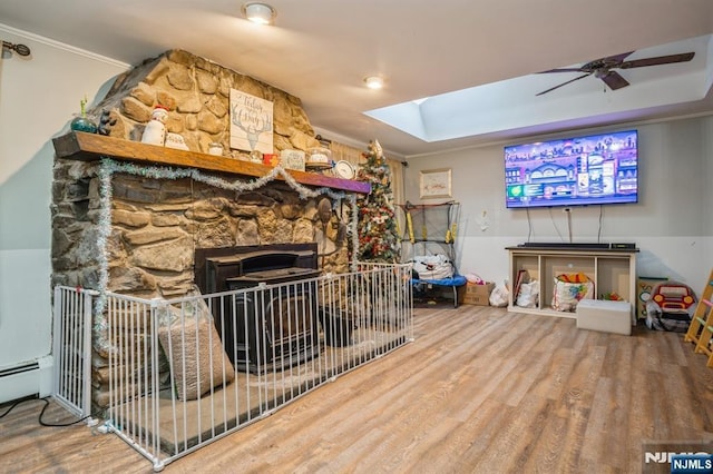 living room featuring hardwood / wood-style flooring, ornamental molding, a stone fireplace, and a skylight