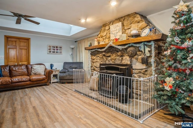 living room featuring hardwood / wood-style flooring, ceiling fan, a skylight, a fireplace, and ornamental molding