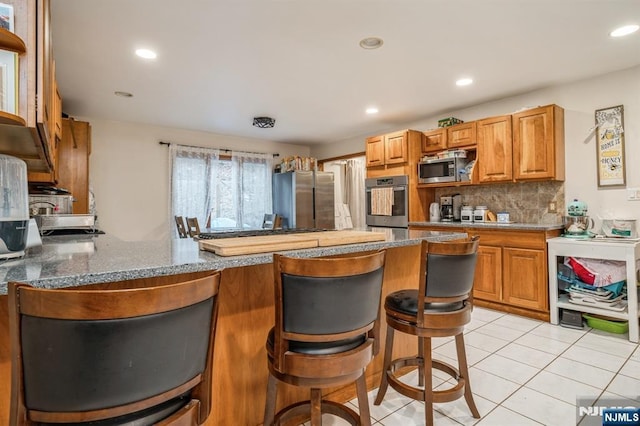 kitchen featuring backsplash, a kitchen breakfast bar, stainless steel appliances, light tile patterned flooring, and kitchen peninsula