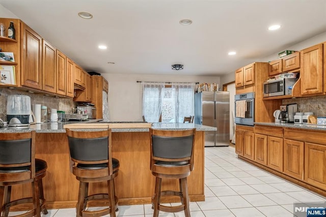 kitchen with light tile patterned floors, appliances with stainless steel finishes, a kitchen breakfast bar, kitchen peninsula, and backsplash