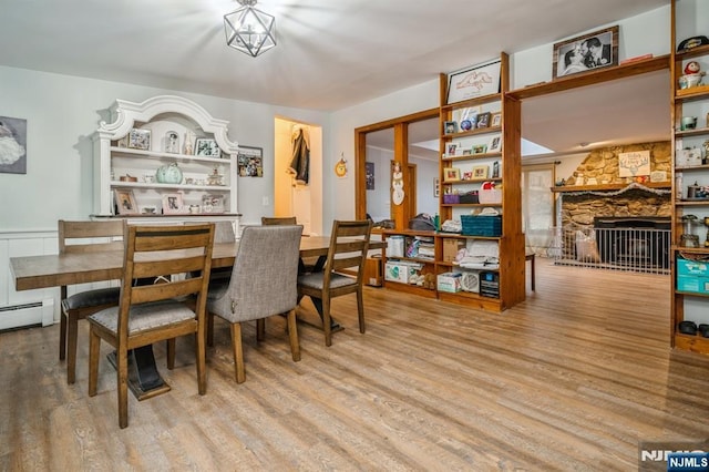 dining room featuring a baseboard radiator, a fireplace, and light hardwood / wood-style floors