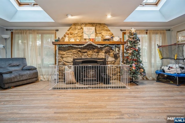 living room with ornamental molding, a stone fireplace, and a skylight