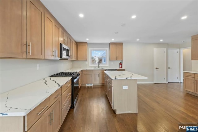 kitchen with appliances with stainless steel finishes, a center island, hardwood / wood-style floors, and light stone counters