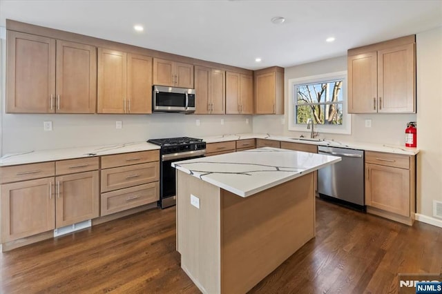 kitchen featuring a kitchen island, sink, stainless steel appliances, light stone countertops, and dark wood-type flooring