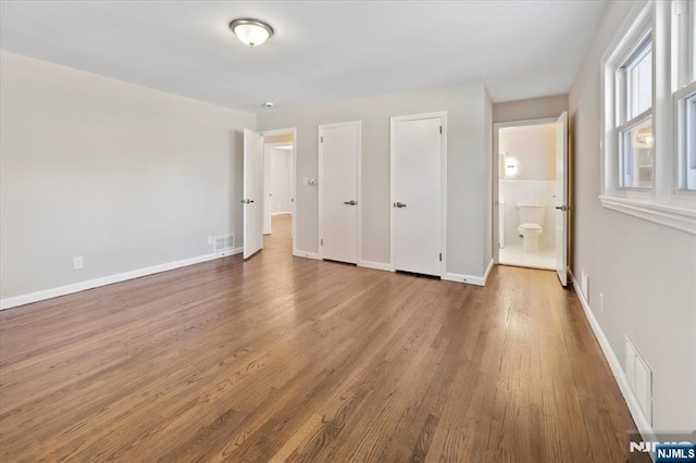 unfurnished bedroom featuring hardwood / wood-style floors, two closets, and ensuite bathroom