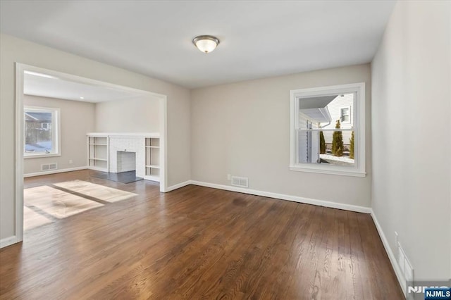 unfurnished living room with dark wood-type flooring and a brick fireplace