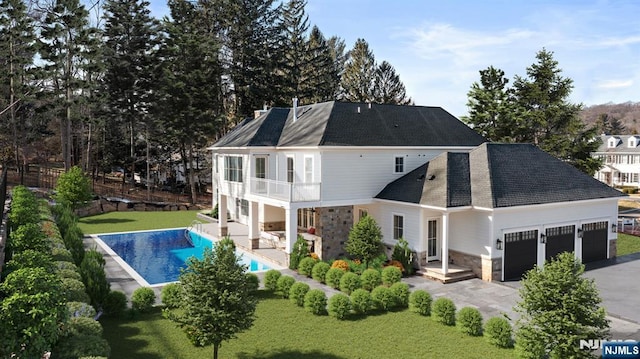 back of property with a balcony, a garage, stone siding, a yard, and an outdoor pool