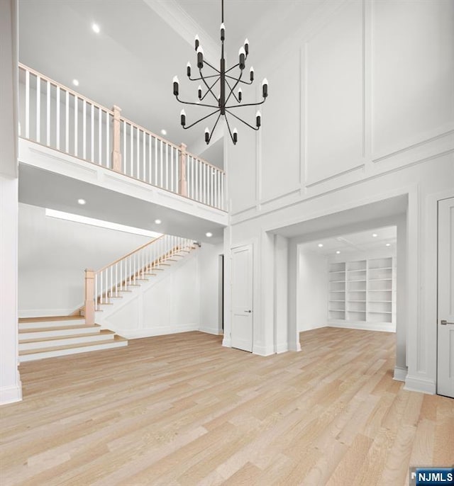 unfurnished living room with built in shelves, stairway, a high ceiling, an inviting chandelier, and light wood-type flooring